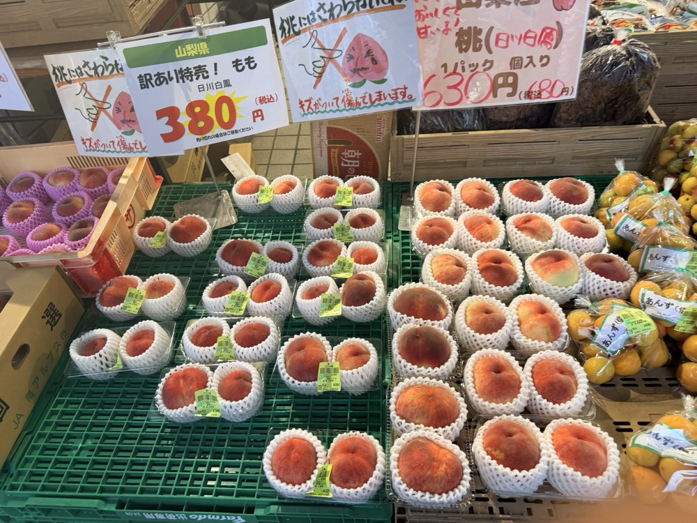 山梨県產桃子的水果攤，價目牌寫著「訳あり特売！もも 380円（税込）」「1パック 個入り」